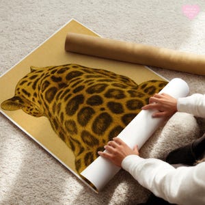 May include: A rolled-up print of a jaguar with a tan and brown spotted pattern. The print is on a tan background, with a rolled-up brown paper tube next to it. The print is being held by a person wearing a white sweater.