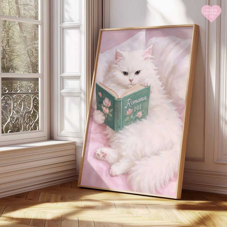 May include: A framed print featuring a fluffy white cat reading a book titled "Romance 101." The cat is lying on a pink surface, with a window and wooden floor in the background. The book has floral illustrations.