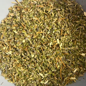 Puede incluir: Primer plano de una mezcla de hierbas y flores secas. La mezcla presenta hojas verdes, capullos florales morados y tallos marrones. Las hierbas están finamente picadas y parecen ser una mezcla de lavanda y otras plantas aromáticas, probablemente para uso culinario o aromaterapia.