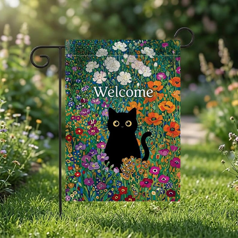 May include: A garden flag featuring a black cat with yellow eyes, surrounded by colorful flowers. The word "Welcome" is displayed in white text. The flag is hanging on a black metal stand, set against a backdrop of green grass and other flowers.