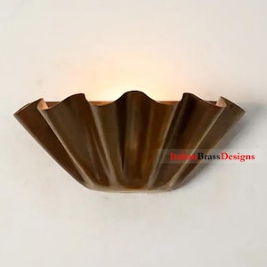 Könnte beinhalten: Bronze-farbene Wandleuchte mit einem gerüschten, blütenblattartigen Design. Die Leuchte ist an einer weißen Wand montiert und strahlt ein warmes Licht aus. Die Leuchte hat eine einzigartige, dekorative Form.