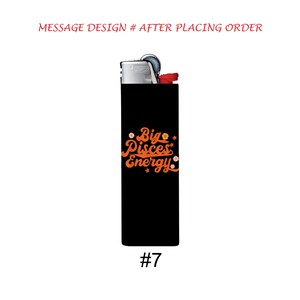 Pu&ograve; includere: Un accendino nero con la scritta "Big Pisces Energy" in arancione. L'accendino ha la parte superiore argentata e un pulsante rosso. Il numero "7" &egrave; stampato in bianco in basso.