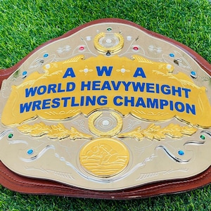 Może przedstawiać: Pas mistrzowski AWA World Heavyweight Wrestling Champion. Złoty i srebrny pas z napisem "AWA WORLD HEAVYWEIGHT WRESTLING CHAMPION" w kolorze niebieskim. Pas ma brązowy skórzany pasek i jest ozdobiony klejnotami.