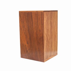 May include: A rectangular wooden box with a rich, dark brown finish. The wood grain is prominently displayed, creating a natural, textured appearance. The box is a solid, upright structure, likely for storage or display.