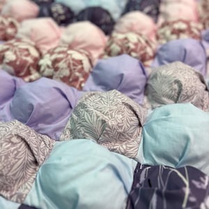 Könnte beinhalten: Nahaufnahme eines Quilts mit Puffstich-Design. Der Quilt zeigt eine Vielzahl von Stoffen in Blau-, Lila- und Rosatönen. Einige Quadrate haben florale Muster, während andere unifarben sind. Der Quilt ist aus weichem Stoff gefertigt.