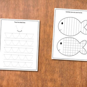 May include: Two white worksheets with black line drawings and text on a wooden surface. One worksheet says "Trace the dotted lines" and features curved lines. The other says "Carefully trace and color the fish" and shows two fish outlines.