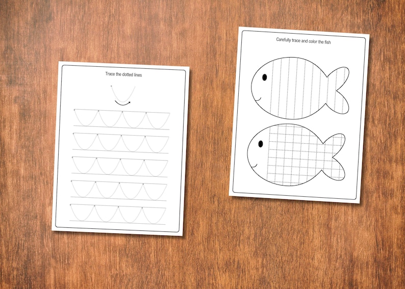 May include: Two white worksheets with black line drawings and text on a wooden surface. One worksheet says "Trace the dotted lines" and features curved lines. The other says "Carefully trace and color the fish" and shows two fish outlines.