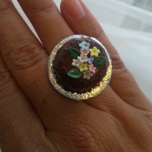May include: A silver ring with a chocolate cake design and colorful flowers on top.