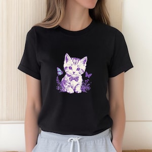 May include: Black t-shirt featuring a purple and white illustration of a kitten wearing a bow tie, with butterflies and floral accents. The graphic is centered on the shirt, creating a cute and whimsical design. The shirt is made of a soft material.