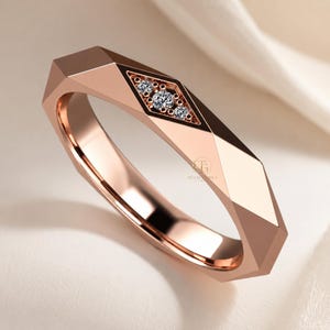 Modern geometric rose gold band ring featuring angular faceted detailing with small round lab grown diamonds set in a central geometric bezel design. Close-up luxury jewelry photo highlights the polished faceted finish, contemporary minimalist craftsmanship, elegant stacking ring style, and refined modern wedding band aesthetic perfect for everyday luxury wear and designer jewelry collections.