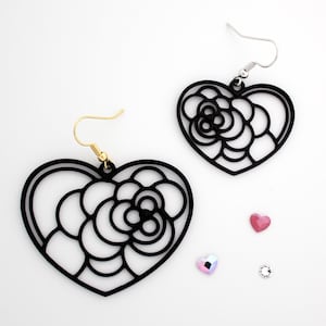 May include: Black heart-shaped earrings with a floral design, featuring gold and silver ear wires. The earrings are displayed with three small heart and round-shaped embellishments on a white background.