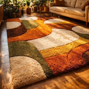 Puede incluir: Una alfombra rectangular de pelo largo y textura afelpada con un patrón geométrico de semicírculos superpuestos y formas curvas en tonos naranja quemado, verde oliva, amarillo mostaza, marrón oscuro y blanco crema.