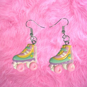 May include: A pair of pastel roller skate earrings. Each earring features a miniature roller skate with a mint green, lavender, yellow, and white design, accented with pink wheels and a silver hook.