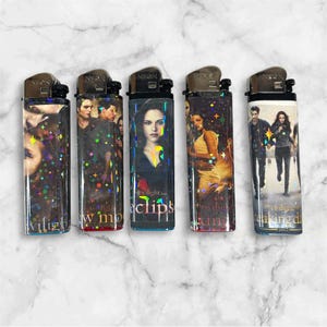 Puede incluir: Cinco encendedores rectangulares con imágenes de la serie de películas Crepúsculo. Cada encendedor tiene una imagen y un texto de película diferentes. Los encendedores están decorados con purpurina iridiscente.