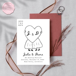 May include: A white save-the-date card with a black heart-shaped illustration featuring the letters "J & D". The card is accompanied by a pink envelope, two silver rings, and a pink wax seal that reads "Merry Marry Studio".