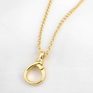May include: A gold-coloured necklace featuring a teardrop or loop-shaped pendant. The fine chain and the pendant are both smooth and shiny. The necklace is presented against a white backdrop.