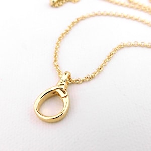 May include: A gold-coloured necklace featuring a pendant in the shape of a loop. The chain is fine and the pendant has a smooth, shiny finish. The necklace is presented against a white backdrop.