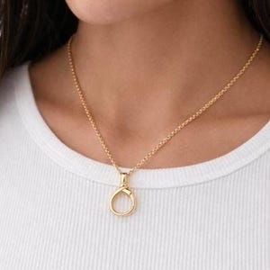 May include: A gold necklace featuring a fine chain and a circular pendant with a clasp design. The necklace is worn against a white top.
