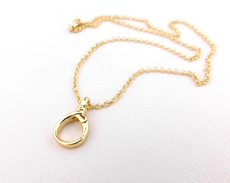 May include: A gold-coloured necklace featuring a pendant in the shape of a loop. The chain is fine and the pendant has a smooth, shiny finish. The necklace is presented against a white backdrop.