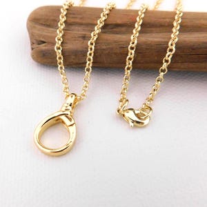 May include: A gold-coloured necklace featuring a lobster clasp and a fine chain. The necklace is presented on a piece of wood against a white backdrop. The chain is composed of small, connected links.