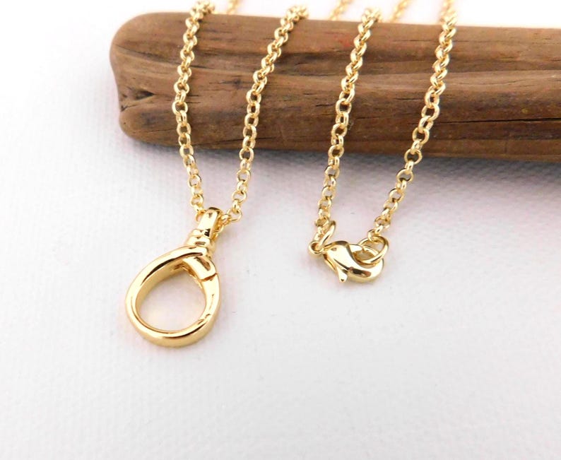 May include: A gold-coloured necklace featuring a lobster clasp and a fine chain. The necklace is presented on a piece of wood against a white backdrop. The chain is composed of small, connected links.