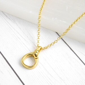 May include: A gold necklace featuring a teardrop-shaped pendant and a delicate chain. The pendant is the focal point, suspended from the chain. The necklace is presented on a white wooden surface, highlighting the gold colour.