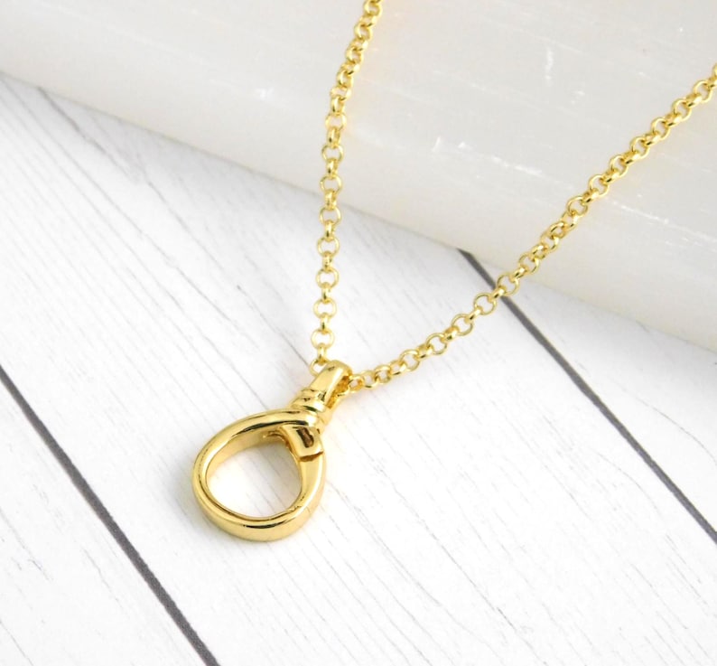 May include: A gold necklace featuring a teardrop-shaped pendant and a delicate chain. The pendant is the focal point, suspended from the chain. The necklace is presented on a white wooden surface, highlighting the gold colour.