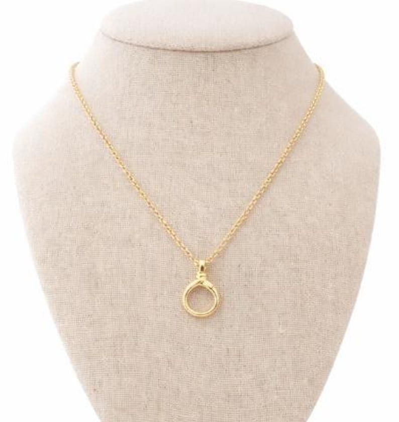 May include: A gold necklace featuring a circular pendant. The pendant is a small, open circle with a clasp at the top, suspended from a fine chain. The necklace is displayed on a beige mannequin.
