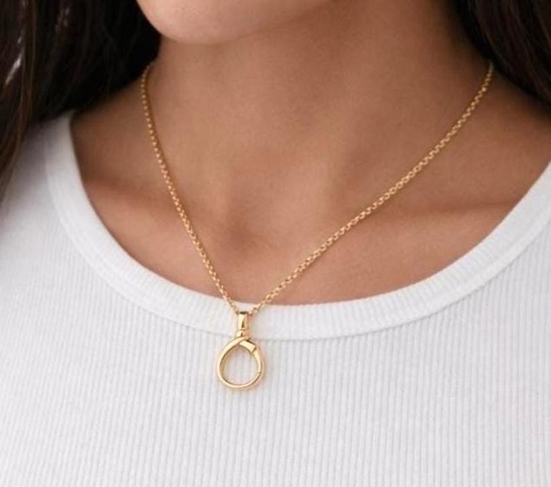 May include: A gold necklace featuring a fine chain and a circular pendant with a clasp design. The necklace is worn against a white top.