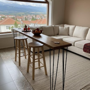 Puede incluir: Una larga mesa de bar de madera con patas de horquilla negras, colocada frente a una gran ventana. Dos taburetes de madera están colocados en la barra. Un cuenco de fruta y un juego de té están sobre la mesa. La habitación tiene una paleta de colores neutros.