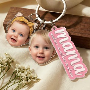 May include: A personalized keychain featuring two baby faces and a pink tag that says "mama" with names. The keychain has a silver ring and is attached to a wooden block. The baby faces are smiling.