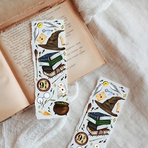 May include: Two decorative bookmarks with a Harry Potter theme. Each bookmark features illustrations of a sorting hat, books, a cauldron, an owl, and the Platform 9 3/4 logo. The bookmarks are set against an open book.