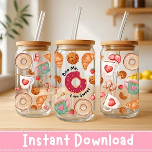Op de afbeelding: Drie glazen drinkbekers met bamboe deksels en doorzichtige rietjes. Elke beker is versierd met aquarel afbeeldingen van donuts, croissants, koekjes, aardbeien en mokken met harten. Eén beker heeft de tekst "Bite Me, I am Sweet".