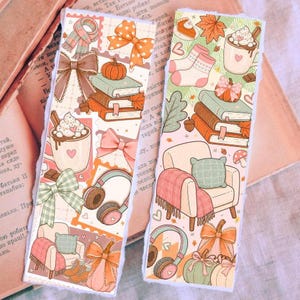Pode incluir: Dois marcadores de página retangulares com um padrão repetitivo de ilustrações com tema de outono, incluindo pilhas de livros, abóboras, canecas de chocolate quente com chantilly, laços, fones de ouvido e poltronas com mantas.
