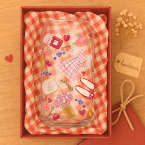 May include: A clear glass can-shaped tumbler with a whimsical design featuring a pink gingham dress, strawberries, roses, and a jar of jam. The tumbler is presented in a red box with a red and white checkered lining, and a "handmade" tag.