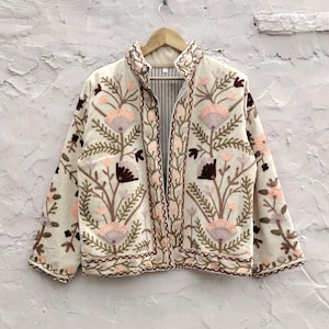 Pode incluir: Casaco bordado creme com um design floral em tons de rosa, castanho e verde. O casaco tem gola alta e forro listrado. O bordado é detalhado e cobre a frente e as mangas.