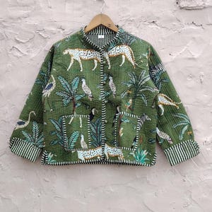 May include: Green quilted jacket with a jungle print of leopards, birds, and palm trees. The jacket has a mandarin collar, button closure, and striped cuffs. The fabric appears lightweight and suitable for layering.