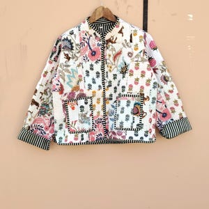 May include: A white quilted jacket with a patchwork design featuring floral and animal motifs in pink, blue, and green. The jacket has a mandarin collar, two front pockets, and black and white striped trim on the cuffs and hem.