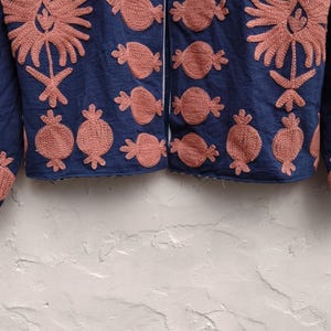 May include: A navy blue jacket with intricate coral-colored embroidery. The design features floral and fruit motifs, creating a textured and visually appealing garment. The jacket's sleeves and front panels are adorned with the detailed embroidery.