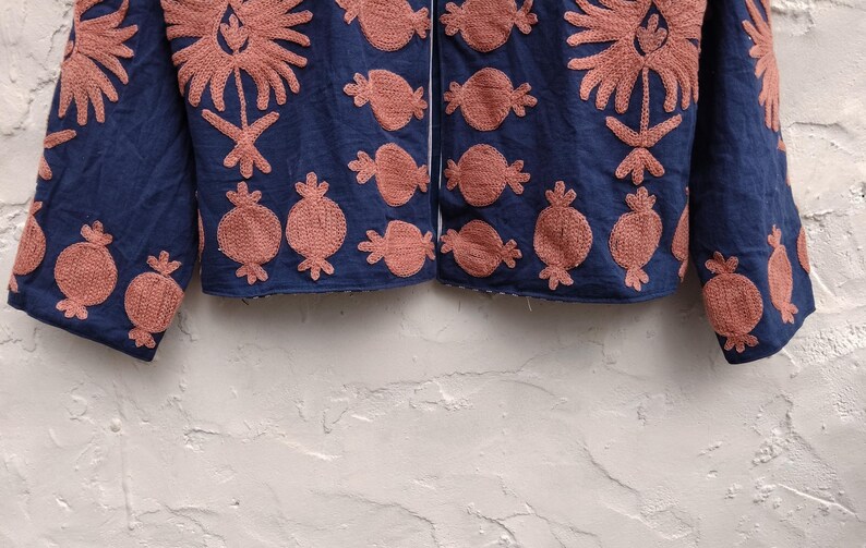 May include: A navy blue jacket with intricate coral-colored embroidery. The design features floral and fruit motifs, creating a textured and visually appealing garment. The jacket's sleeves and front panels are adorned with the detailed embroidery.