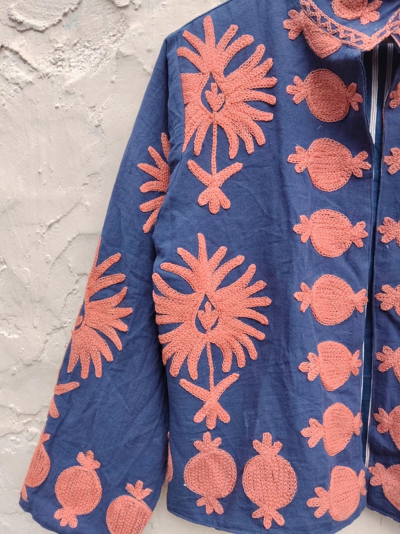 May include: A blue jacket with coral-colored embroidered floral and fruit designs. The jacket features long sleeves and a collared neckline. The embroidery is detailed and covers the front, sleeves, and collar of the jacket.