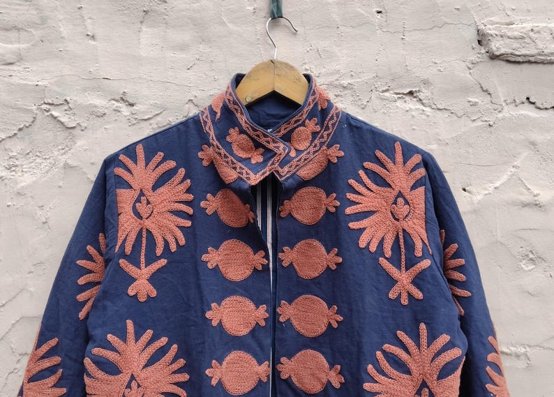 May include: A navy blue jacket with intricate coral-colored embroidery. The jacket features a collared neckline and a series of floral and abstract designs. The embroidery is detailed and covers the front and collar of the jacket.