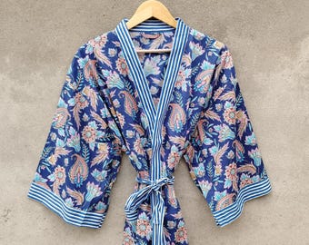 May include: A blue floral print robe with a paisley design. The robe has a striped trim and a matching tie belt. The robe is hanging on a wooden hanger against a neutral background.