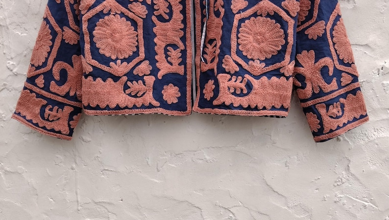 以下が含まれることがあります： ネイビーブルーのジャケット。サンゴ色の刺繍が施されており、花柄や幾何学模様が特徴的で、テクスチャードデザインを作り出しています。 ジャケットはジッパーフロントと長袖で、色とテクスチャの組み合わせを表現しています。