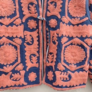 以下が含まれることがあります： ネイビーブルーのジャケット。サンゴ色の刺繍が施されており、結び紐で留めるデザイン。裏地はストライプ柄。刺繍は花柄や幾何学模様で、細部までこだわったテクスチャードデザイン。