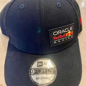 Könnte beinhalten: Verstellbare marineblaue Baseballkappe mit dem Text "ORACLE Red Bull RACING" auf einem Aufnäher. Die Kappe hat einen gebogenen Schirm und einen "9FORTY"-Aufkleber. Hergestellt von New Era.
