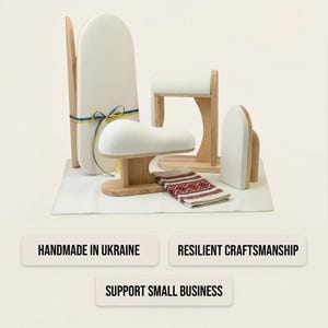 Może przedstawiać: Zestaw drewnianych narzędzi krawieckich obejmujący wysoką deskę do prasowania, rękawnik oraz poduszkę krawiecką, wszystkie pokryte białą tkaniną. Wysoka deska posiada niebiesko-ż&oacute;łtą wstążkę. Dołączona jest mała ściereczka w czerwono-czarny wz&oacute;r geometryczny.