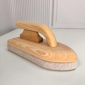 Op de afbeelding: Een houten wasbord met een gebogen handvat en een lichtgekleurde, getextureerde pad. Het bord is gemaakt van lichtgekleurd hout, dat de natuurlijke nerf laat zien. De handgreep is ergonomisch ontworpen.