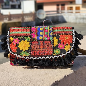 Può includere: Pochette nera con ricami floreali colorati e design patchwork. Presenta dettagli rossi, gialli, rosa e blu, nappe nere e bordatura di perline bianche. Un accessorio unico.