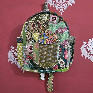 May include: A patchwork backpack with a variety of green, pink, and blue patterned fabrics. The backpack has a rounded top, a front pocket, and adjustable straps. The background is a solid red color with a white floral design.